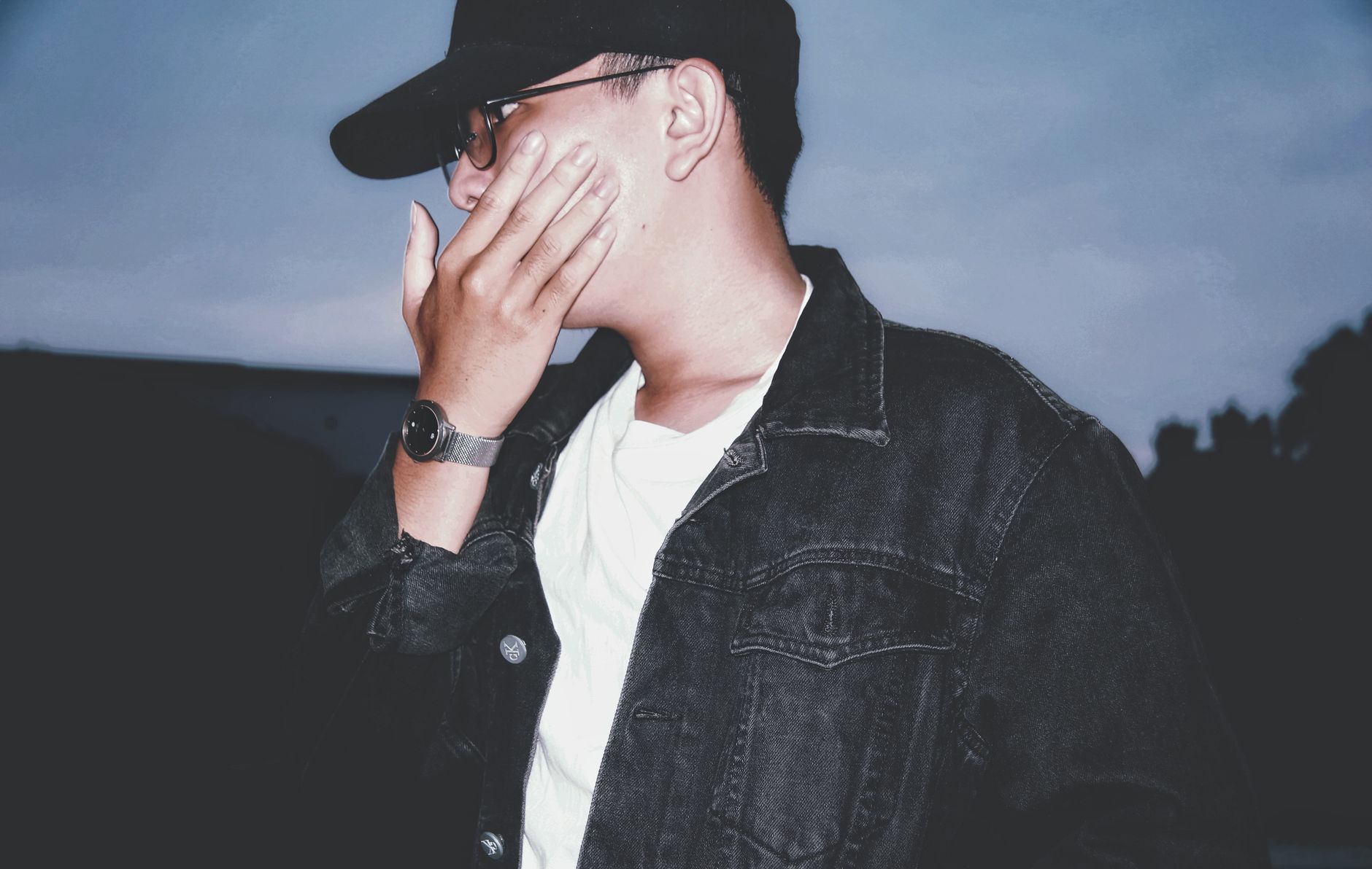 Confident teenage boy in trendy streetwear and sunglasses posing in front of a blurred city at night, styled like a social media profile image with a subtle username area to suggest a cool, attitude-filled boy name.