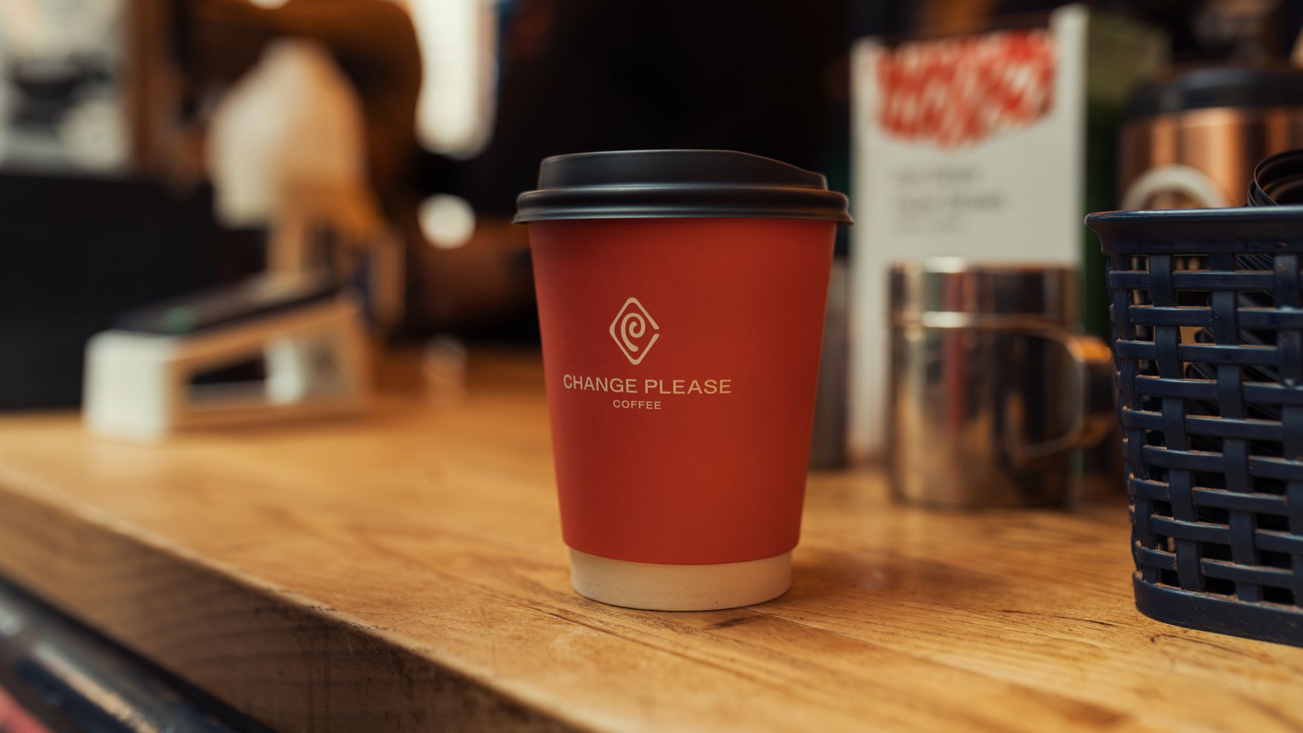 A modern coffee shop counter with an unbranded takeaway cup and paper bag showing a blank circular logo area for creating unique cafe name and logo designs.