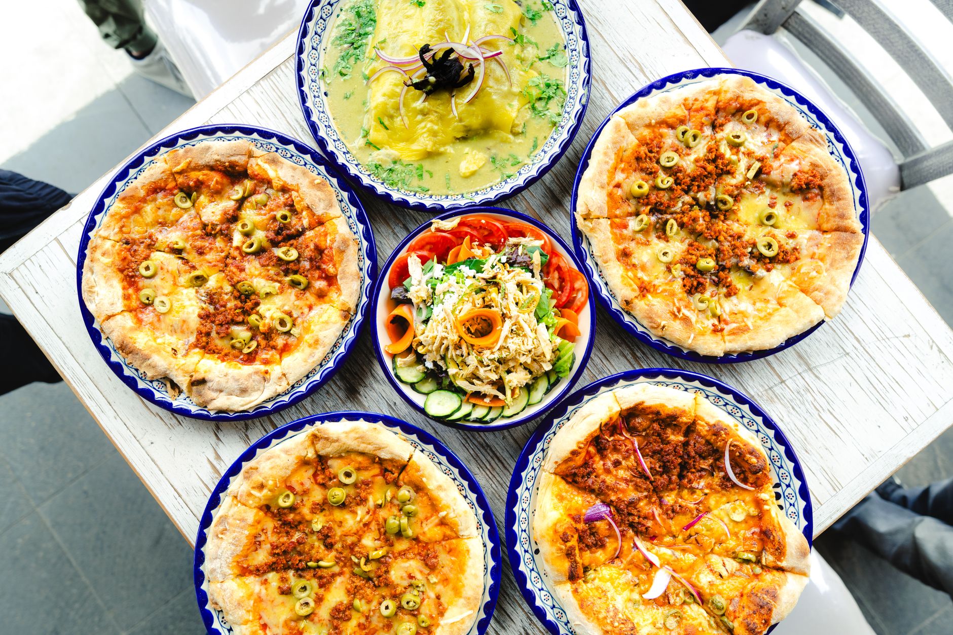 Overhead photo of several people assembling their own pizzas at a topping bar with bowls of different ingredients on a counter.