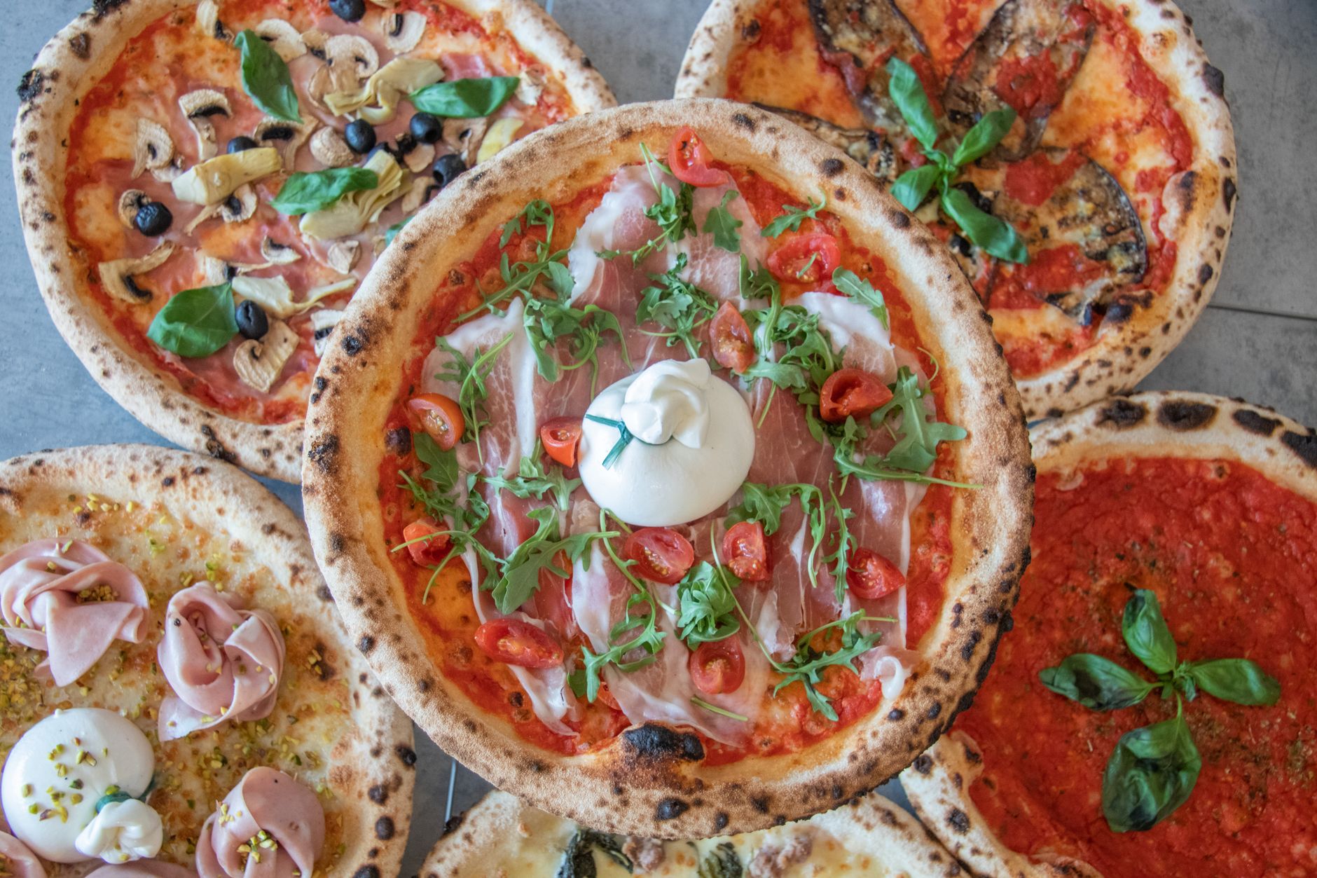 Top-down view of a wooden board displaying various pizza toppings in small piles, including meats, vegetables, cheese, and sauce.